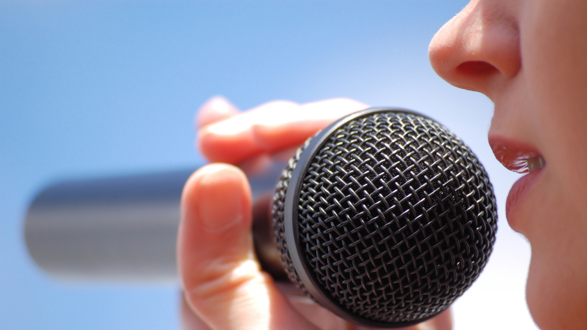 Eine Frau spricht in ein Mikrofon, das sie in der Hand hält.