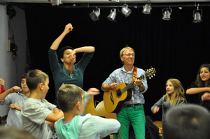Momentaufnahme auf einem Karibuni-Konzert Der Musiker Pit Budde spielt Gitarre. Die Sängerin Josephine Kronfli bewegt ihre Arme und das junge Publikum macht es ihr nach.
