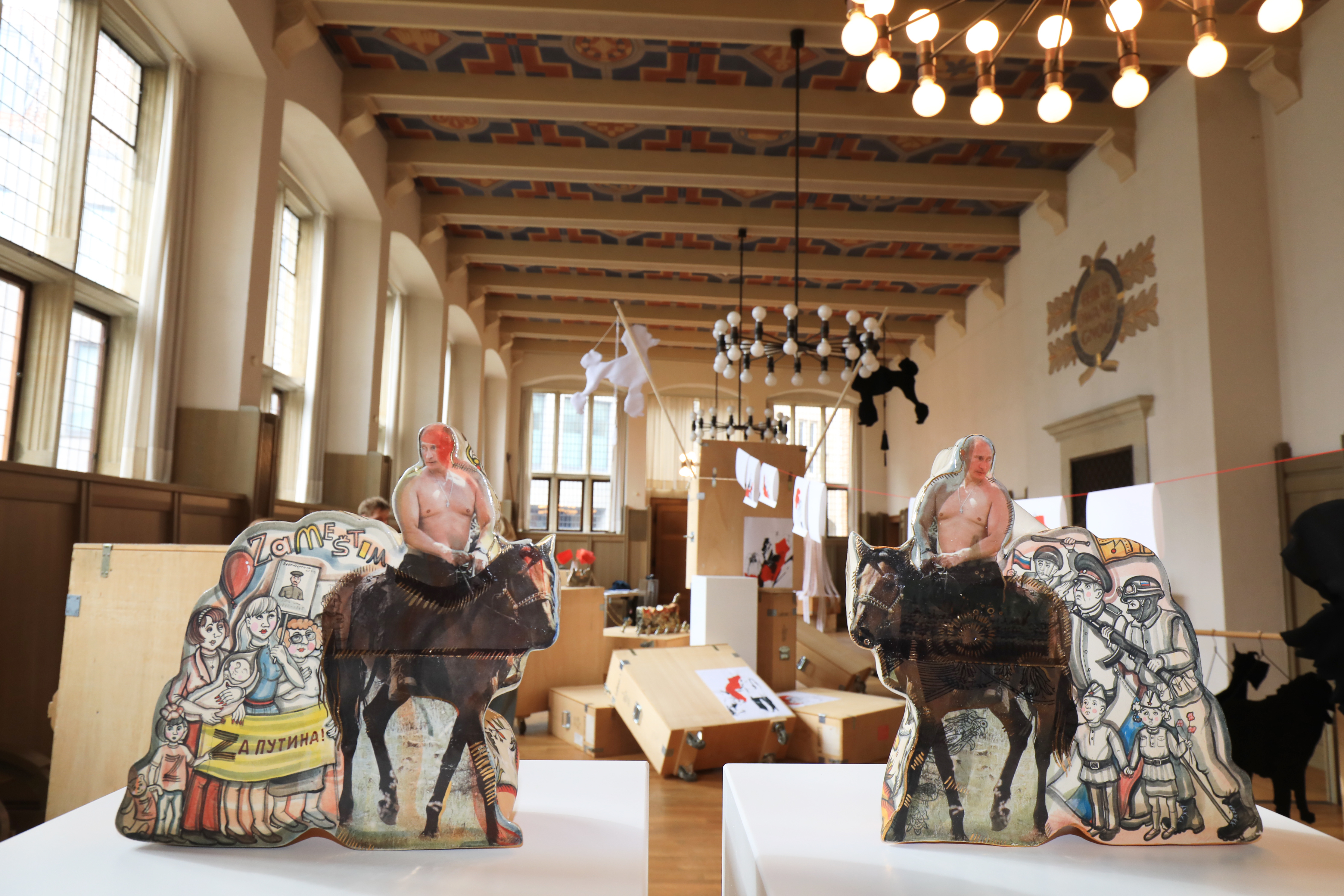 Zwei Skulpturen im Vordergrund jeweils auf einem Tisch oder Podest stehend, dahinter im Hintergrund weitere Teile der Ausstellung.