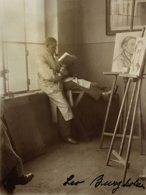 Leo Burgholz in einem Atelier. Er liest und raucht Pfeife
