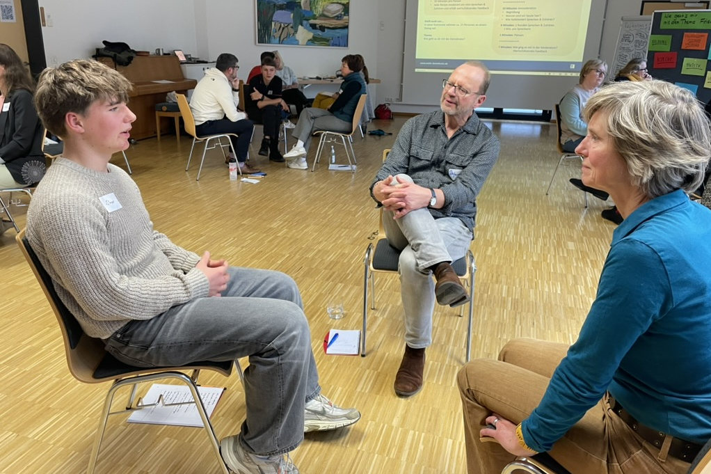 Drei Menschen sitzen sich gegenüber und unterhalten sich.