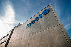 Aufragende Gebäudeecke des Batterieforschungszentrums MEET in Sichtbeton mit dem blauen Schriftzug MEET und Logo