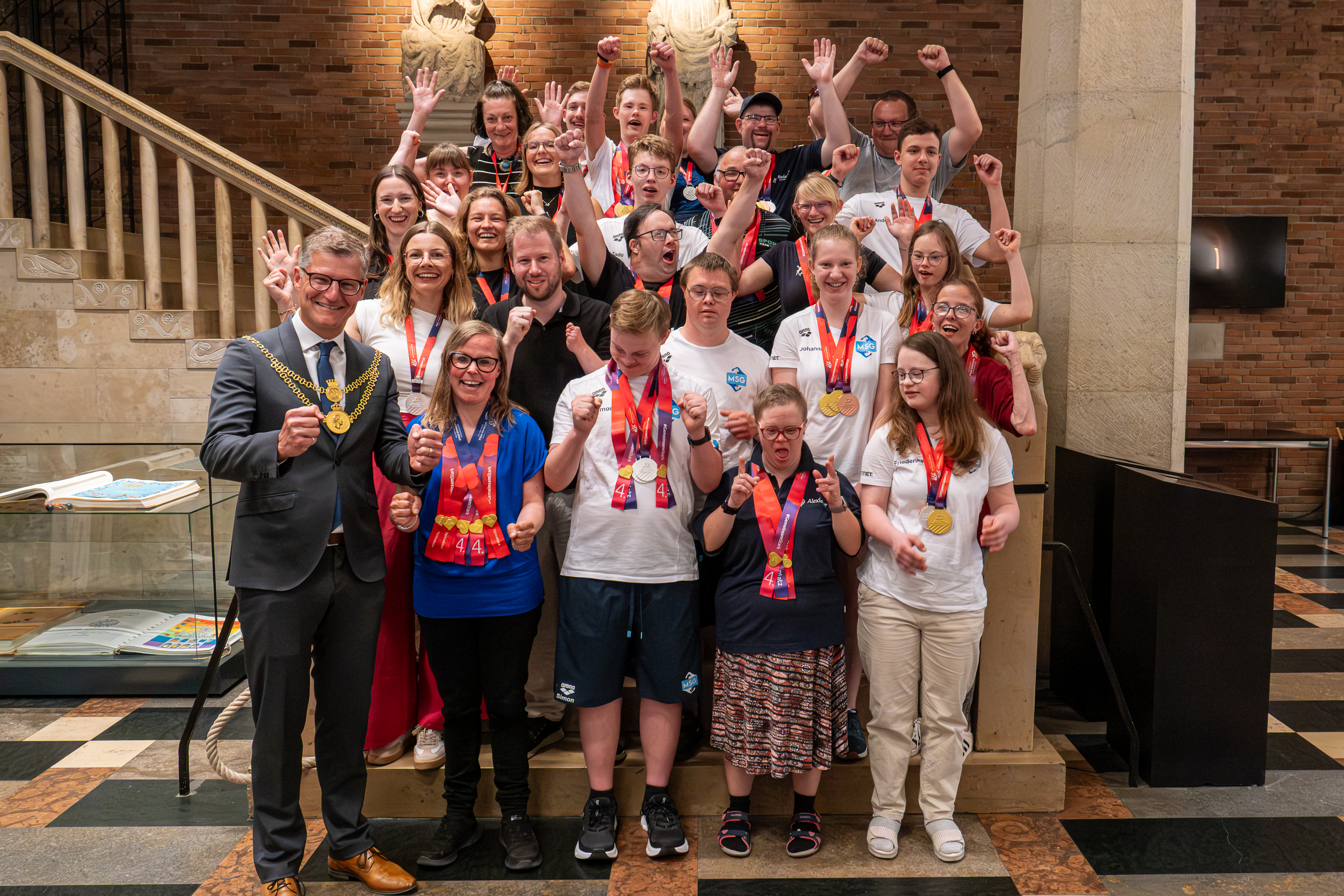 Special-Olympics-Teilnehmenden stehen zusammen mit ihren Begleitenden auf einer Treppe im Rathaus zusammen mit Oberbürgermeister Tilman Fuchs