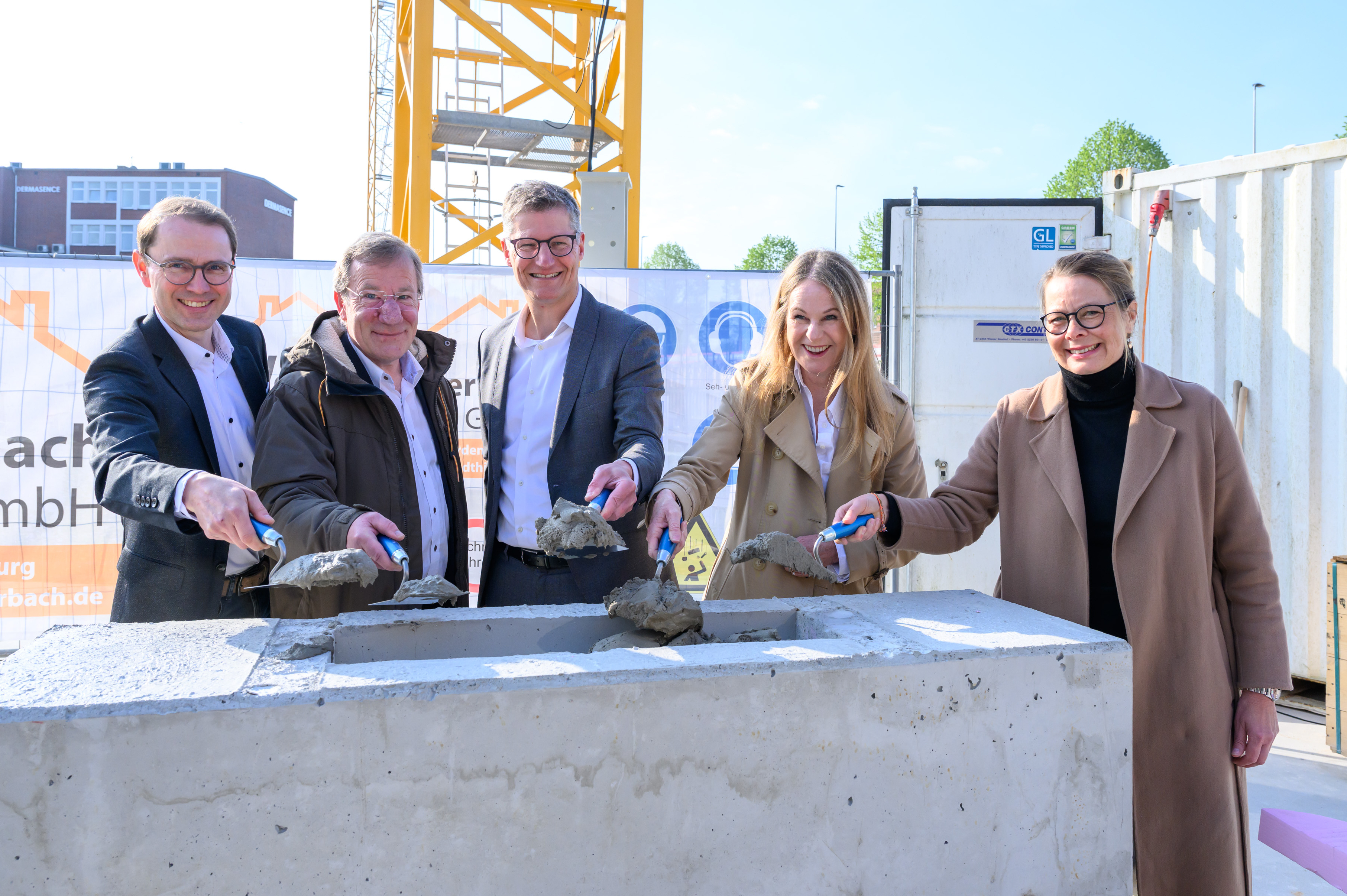 Gruppenfoto von fünf Personen, die mit einer kleinen Schaufel Sand in einen Stein schaufeln