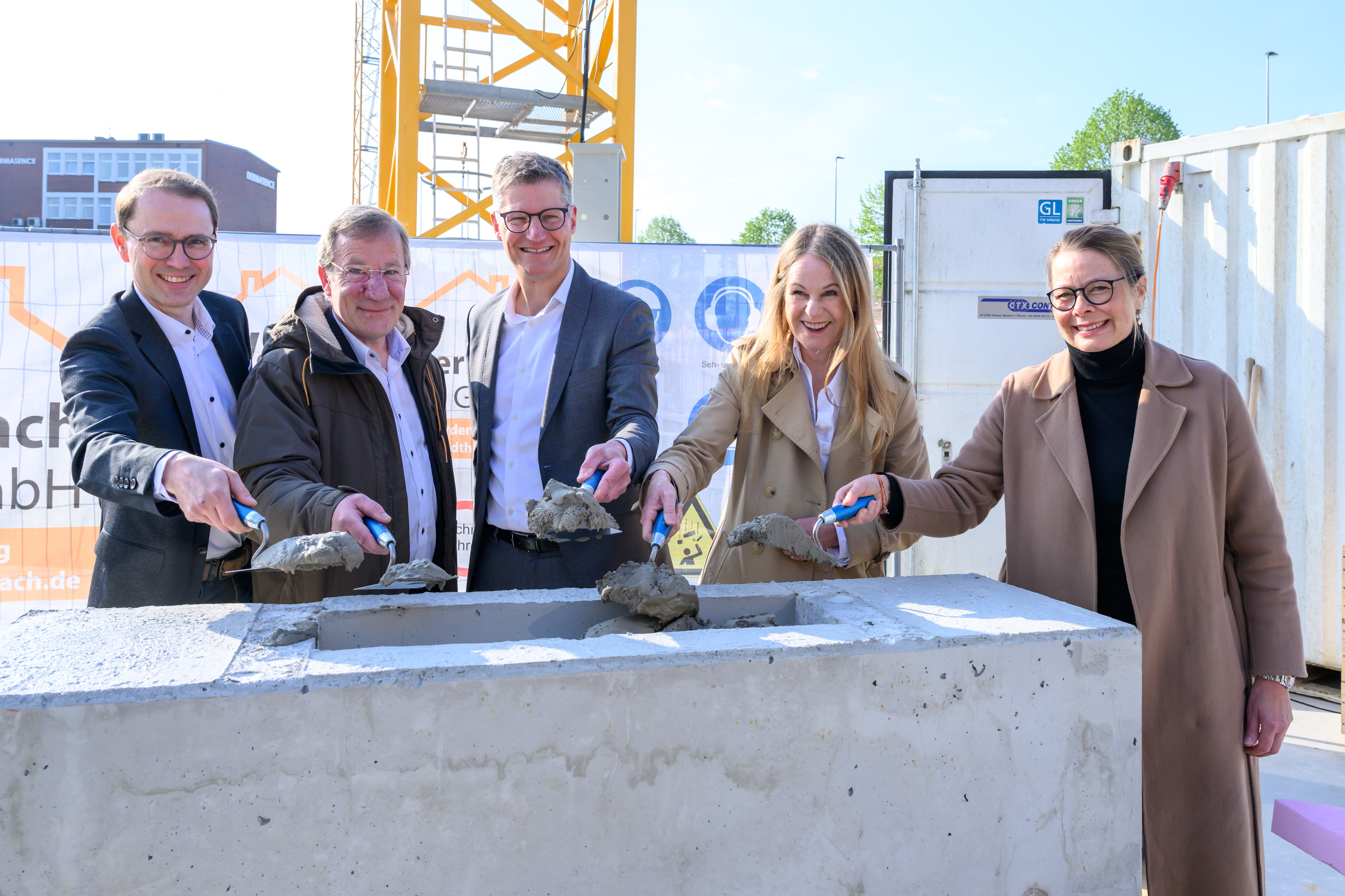 Gruppenfoto von fünf Personen, die mit einer kleinen Schaufel Sand in einen Stein schaufeln