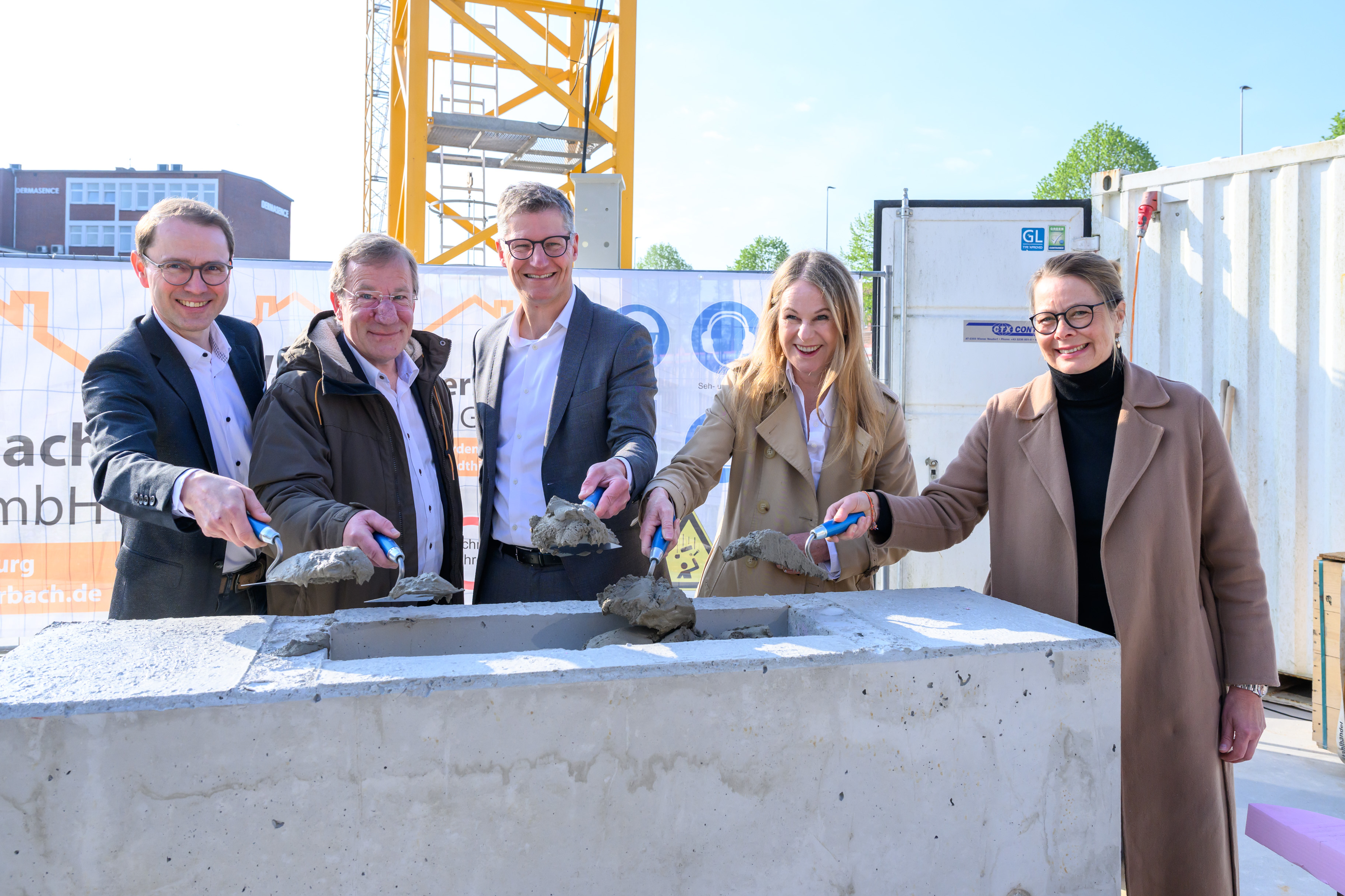 Gruppenfoto von fünf Personen, die mit einer kleinen Schaufel Sand in einen Stein schaufeln