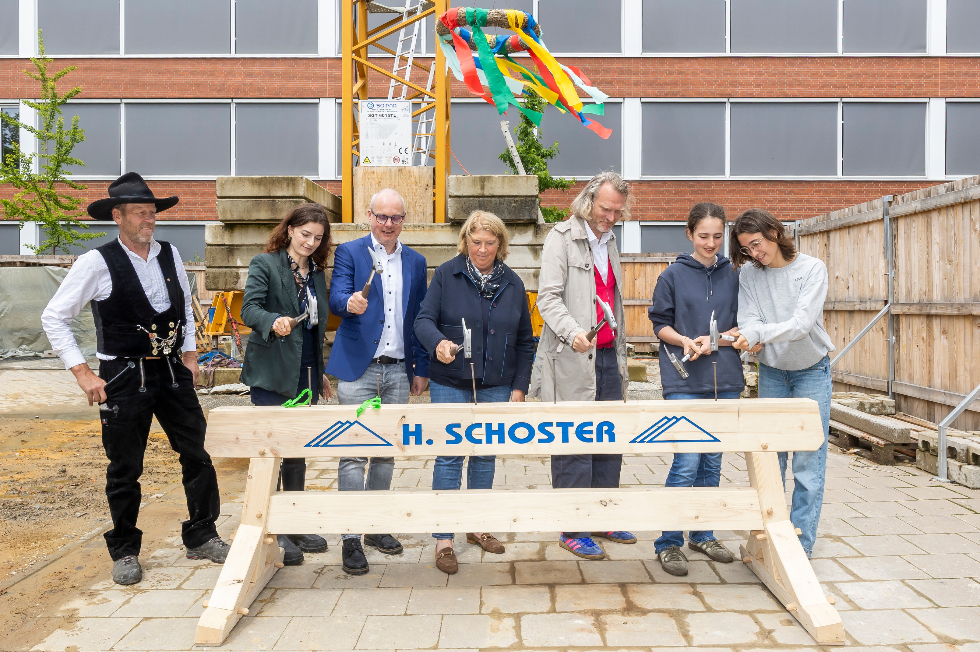 Sieben Personen schlagen symbolisch Nägel in einen Holzbalken