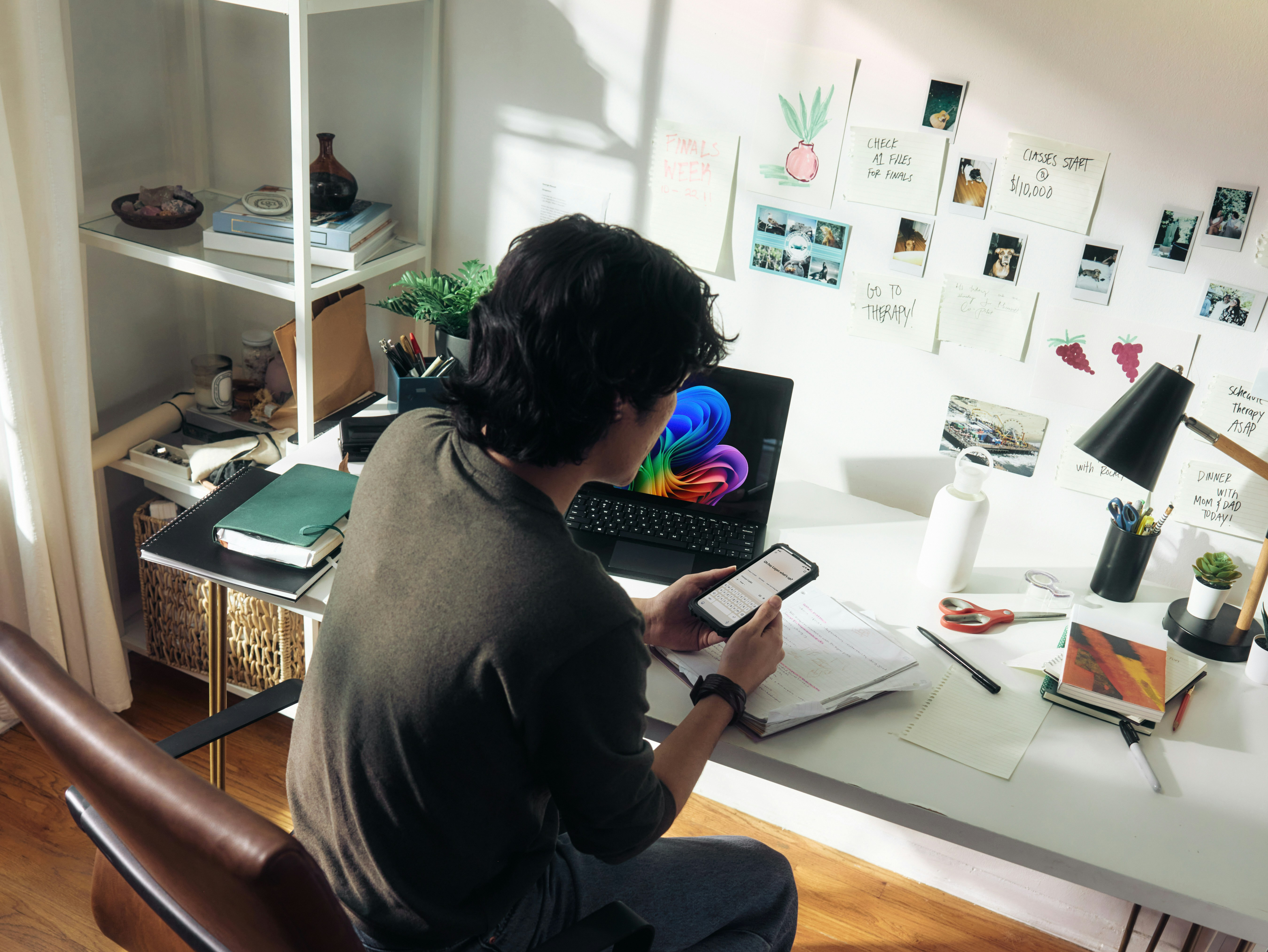 Person mit Smartphone und Laptop an einem Schreibtisch 