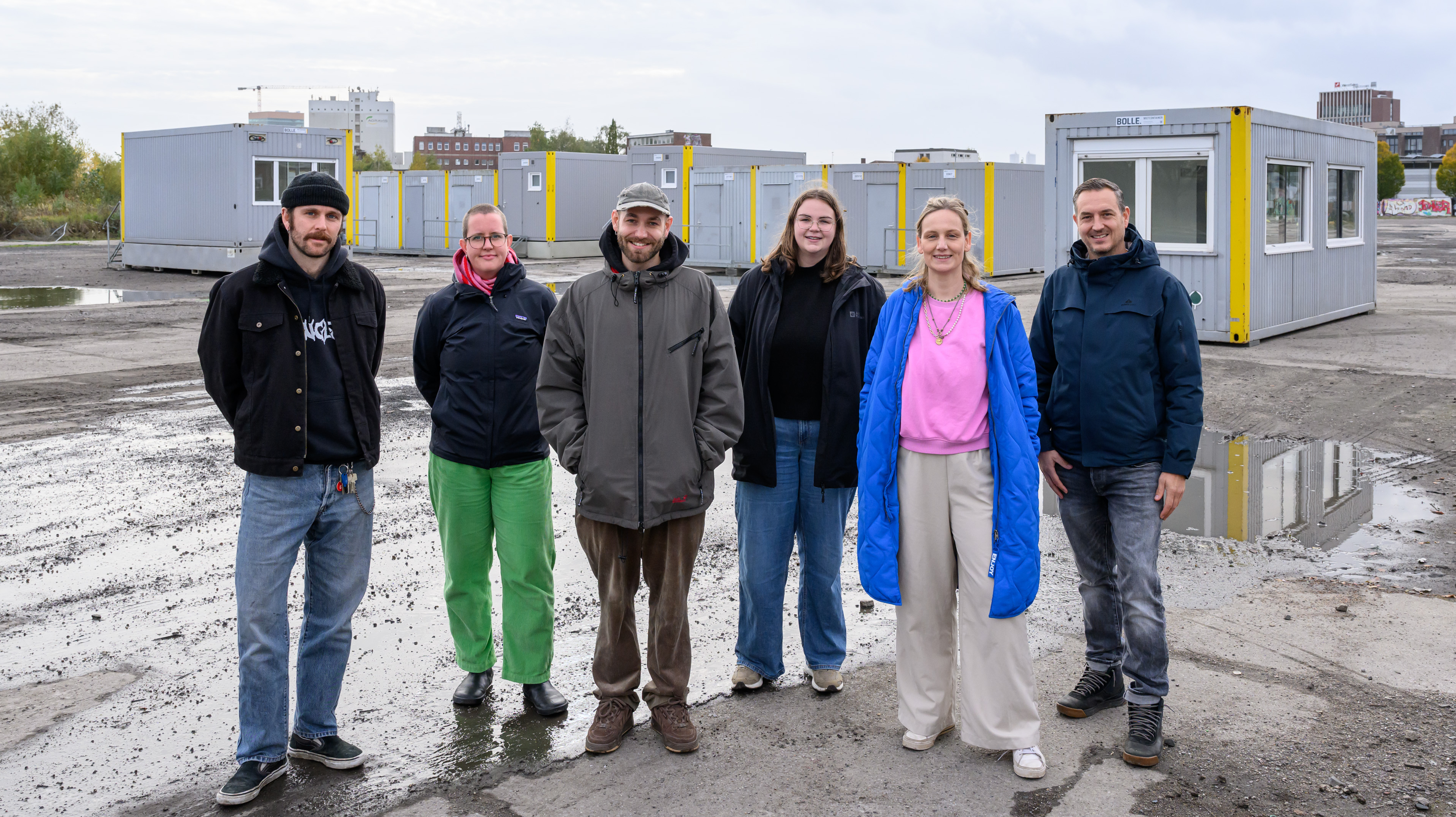 Gruppenfoto von sechs Personen; im Hintergrund stehen Container auf einer freien Fläche