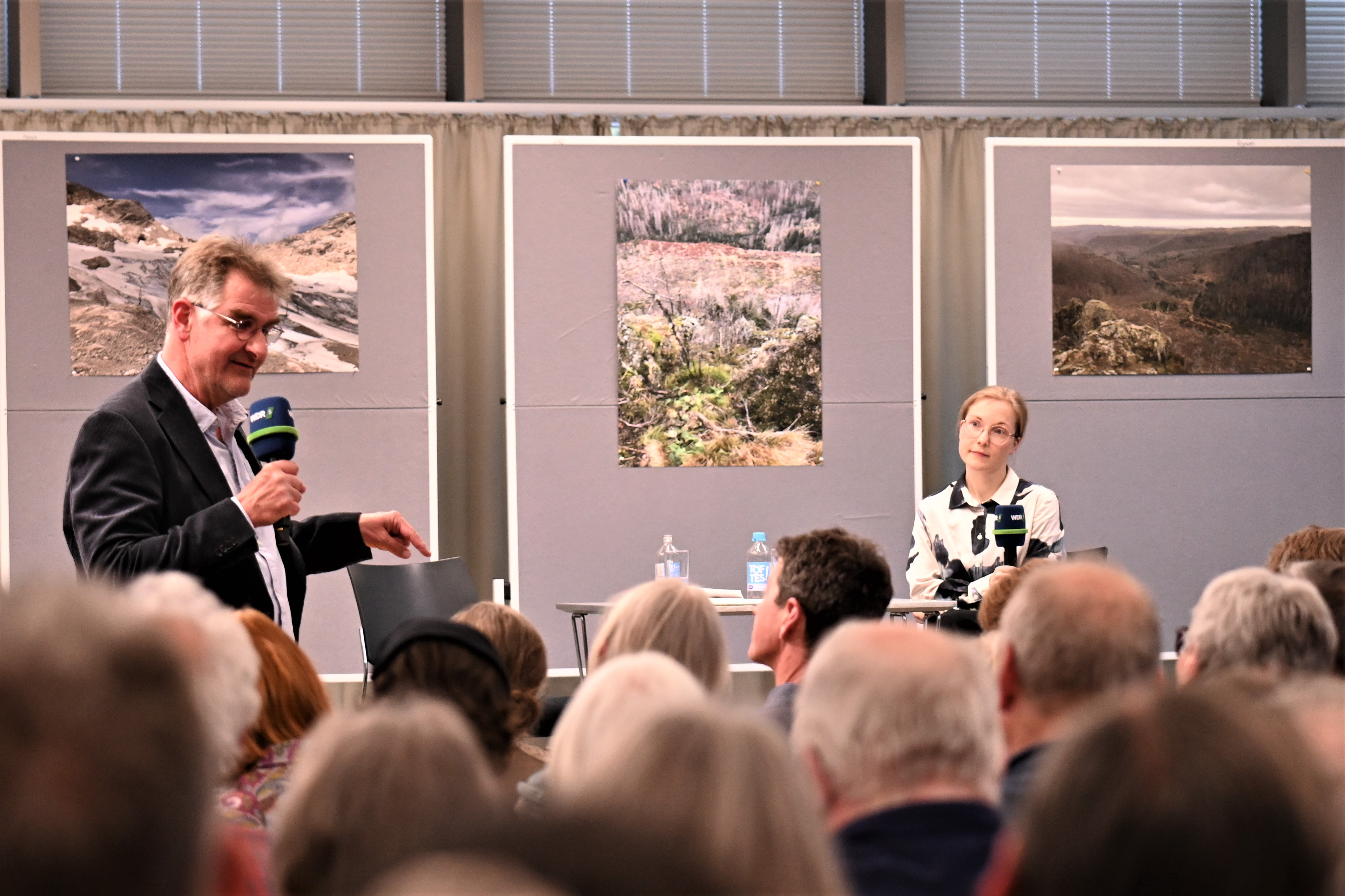 Moderator Jürgen Wiebicke steht mit dem Mikrofon vor einem sitzenden Publikum