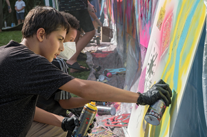 Zwei Jugendliche besprühen eine Spannplatte mit Graffity-Farben