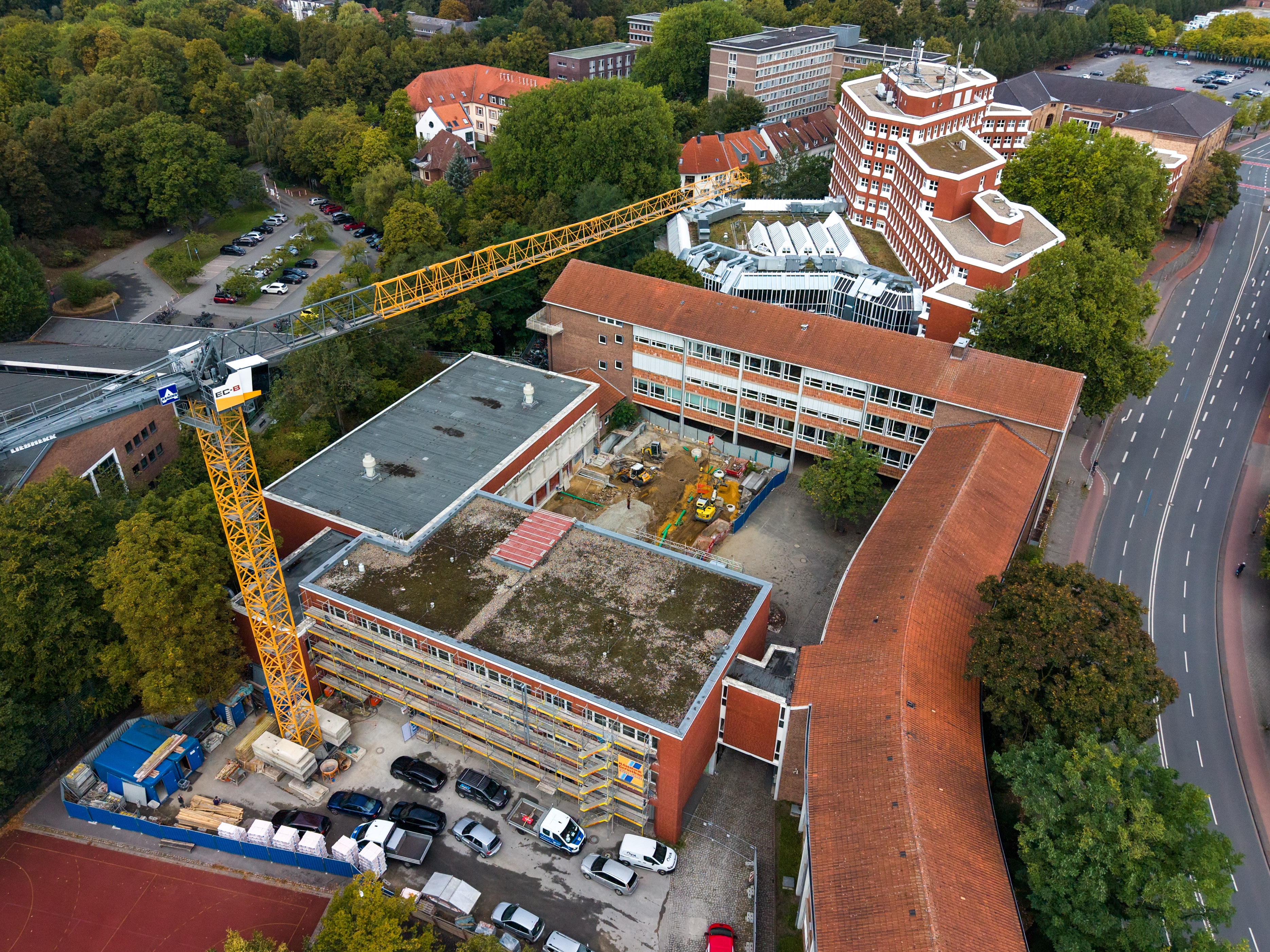 Drohnenaufnahme: Blick auf die Schule von oben. Links steht noch ein Baukran. Außerdem sind grüne Bäume zu sehen. 