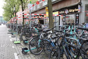 Rechts im Bild ist eine Ladenstraße abgebildet, davor eine Reihe von parkenden Fahrrädern und E-Scootern, die die Zugänge zu den dahinterliegenden Geschäften blockieren. Zukünftig sind hier Parkmarkierungen vorgesehen, damit die Zugänge zu den Geschäften zukünftig frei bleiben. 