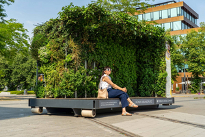 Frau mit Sonnenbrille sitzt vor einer großen, begrünten, mobilen Pflanzenwand in einem urbanen Umfeld