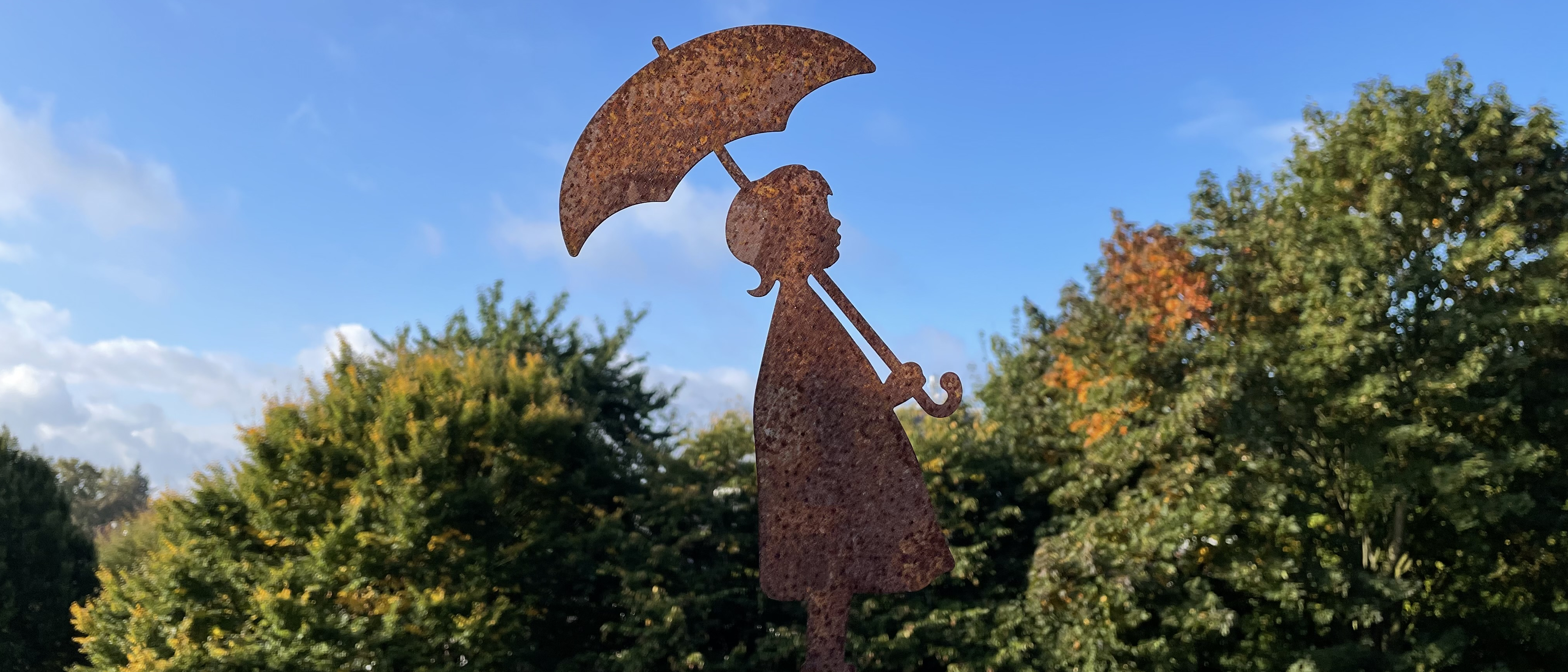 Figur (Mädchen mit Regenschirm) vor blauem Himmel und Herbstbäumen