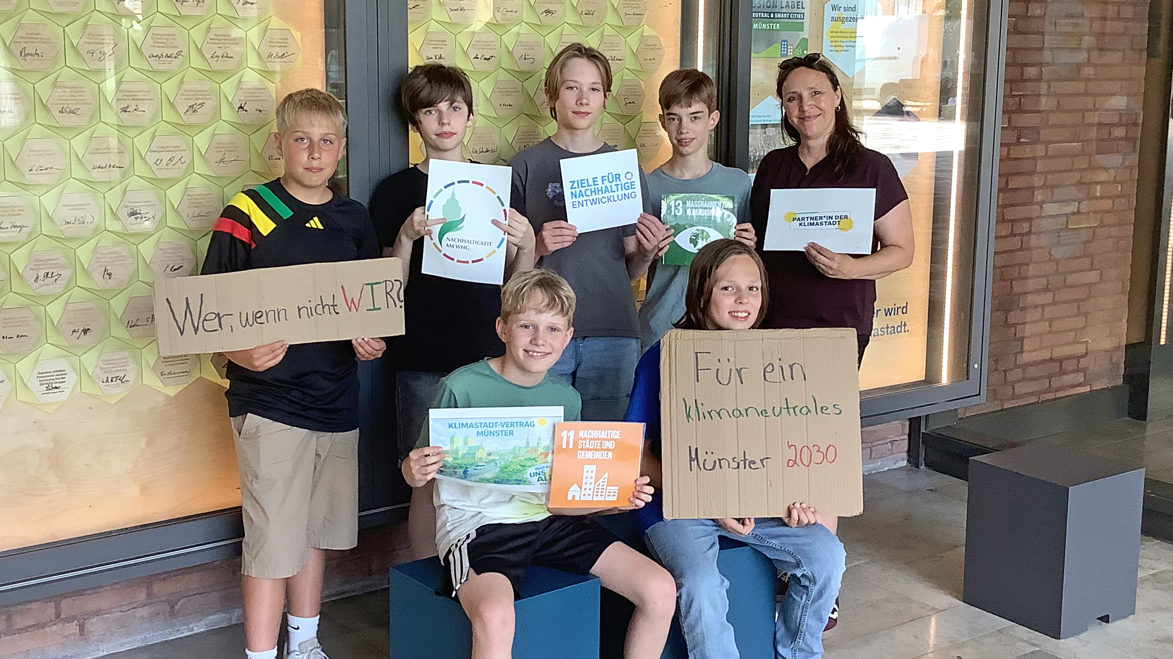 Schüler des Hittorf-Gymnasiums stehen vor der Klimastadtvertrag Wand zusammen mit ihrer Lehrerin