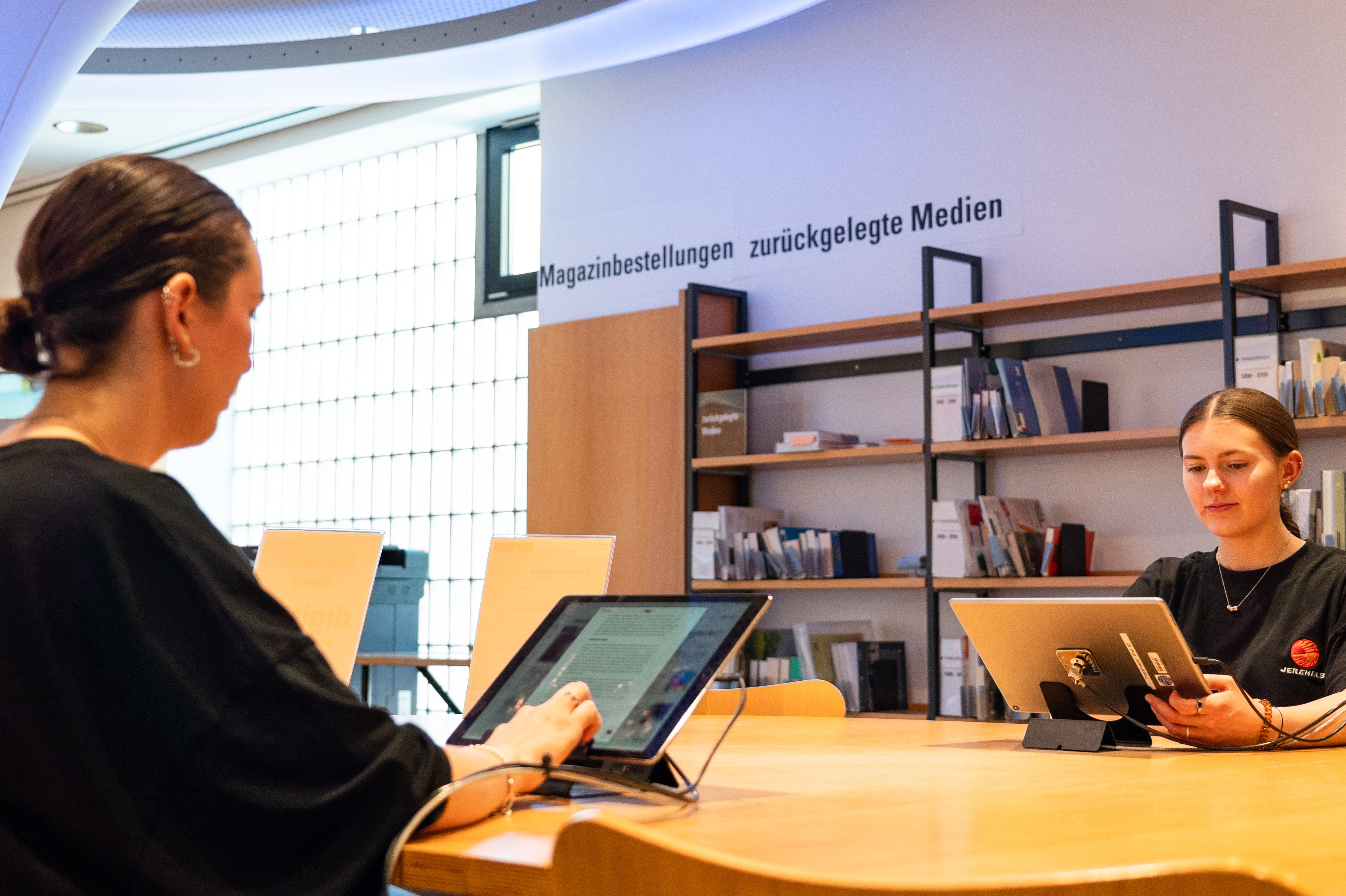 Zwei Frauen sitzen an einem Tisch und lesen auf einem Tablet