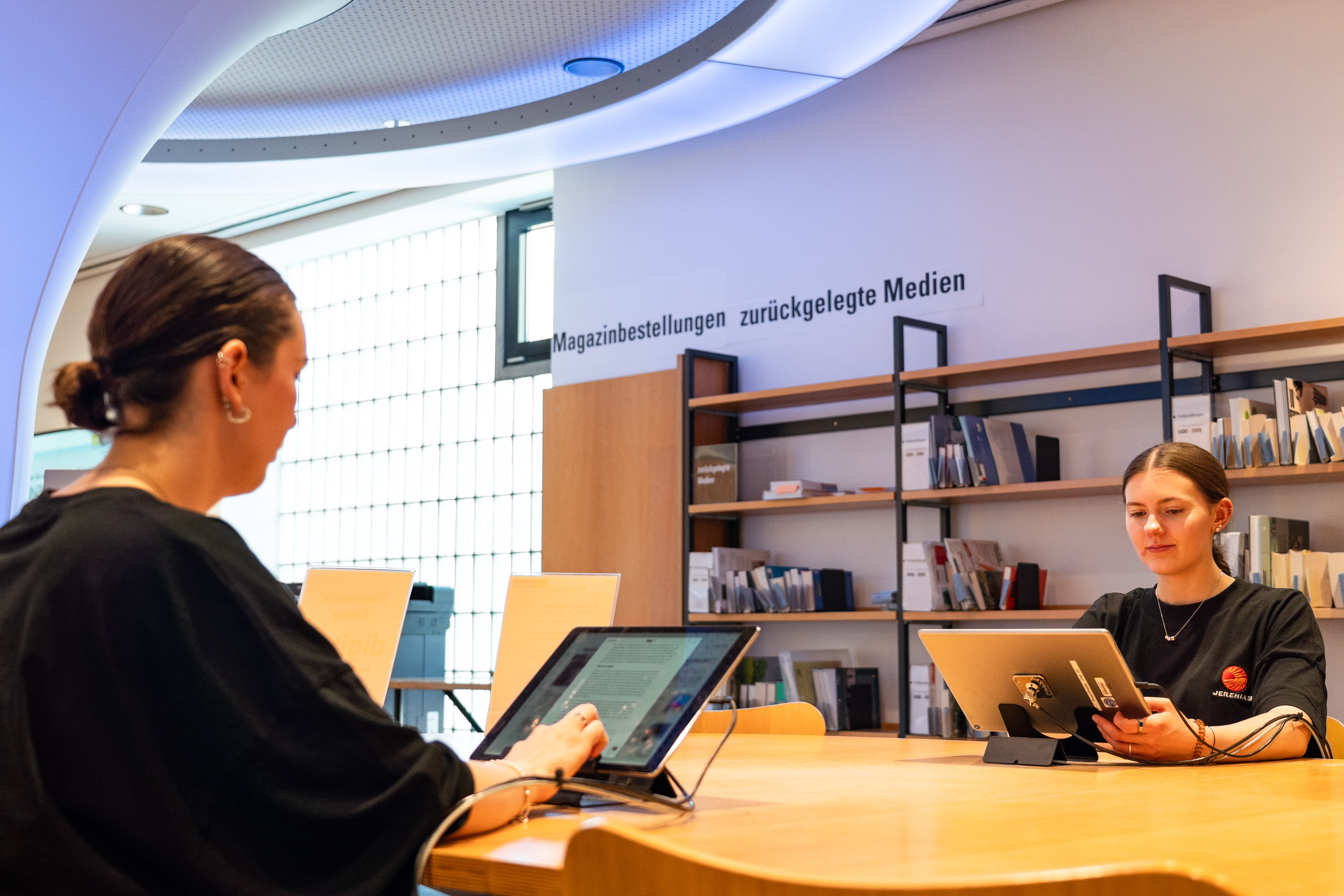 Zwei Frauen sitzen an einem Tisch und lesen auf einem Tablet