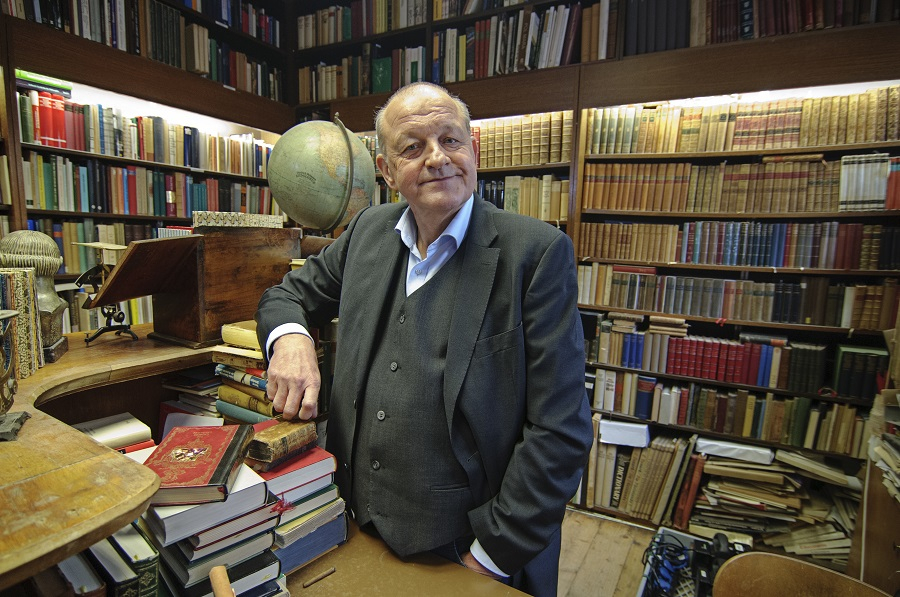 Leonard Lansink steht im Antiquariat umgeben von Büchern