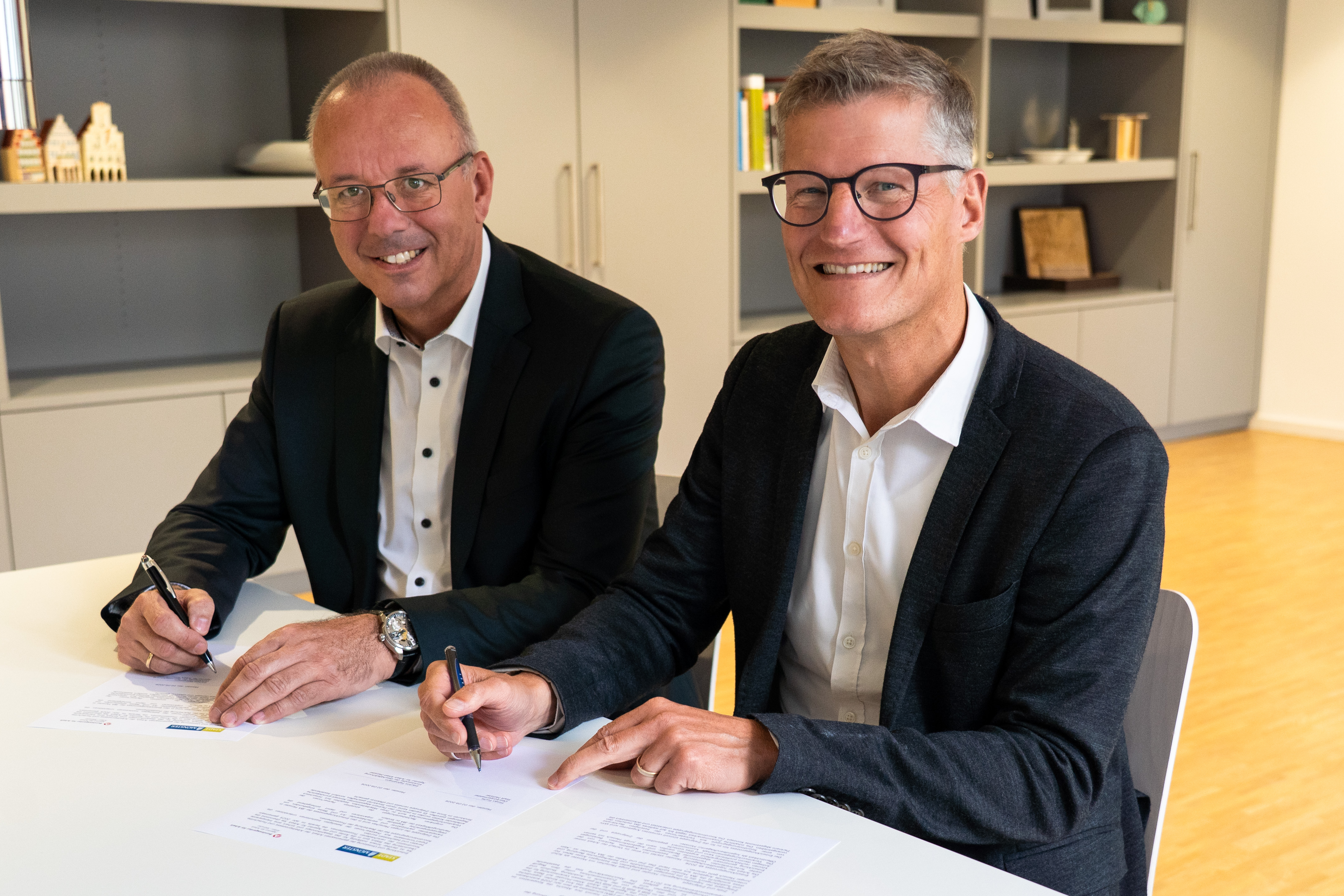 Zwei Personen sitzen nebeneinander an einem Tisch und schreiben auf Papier.