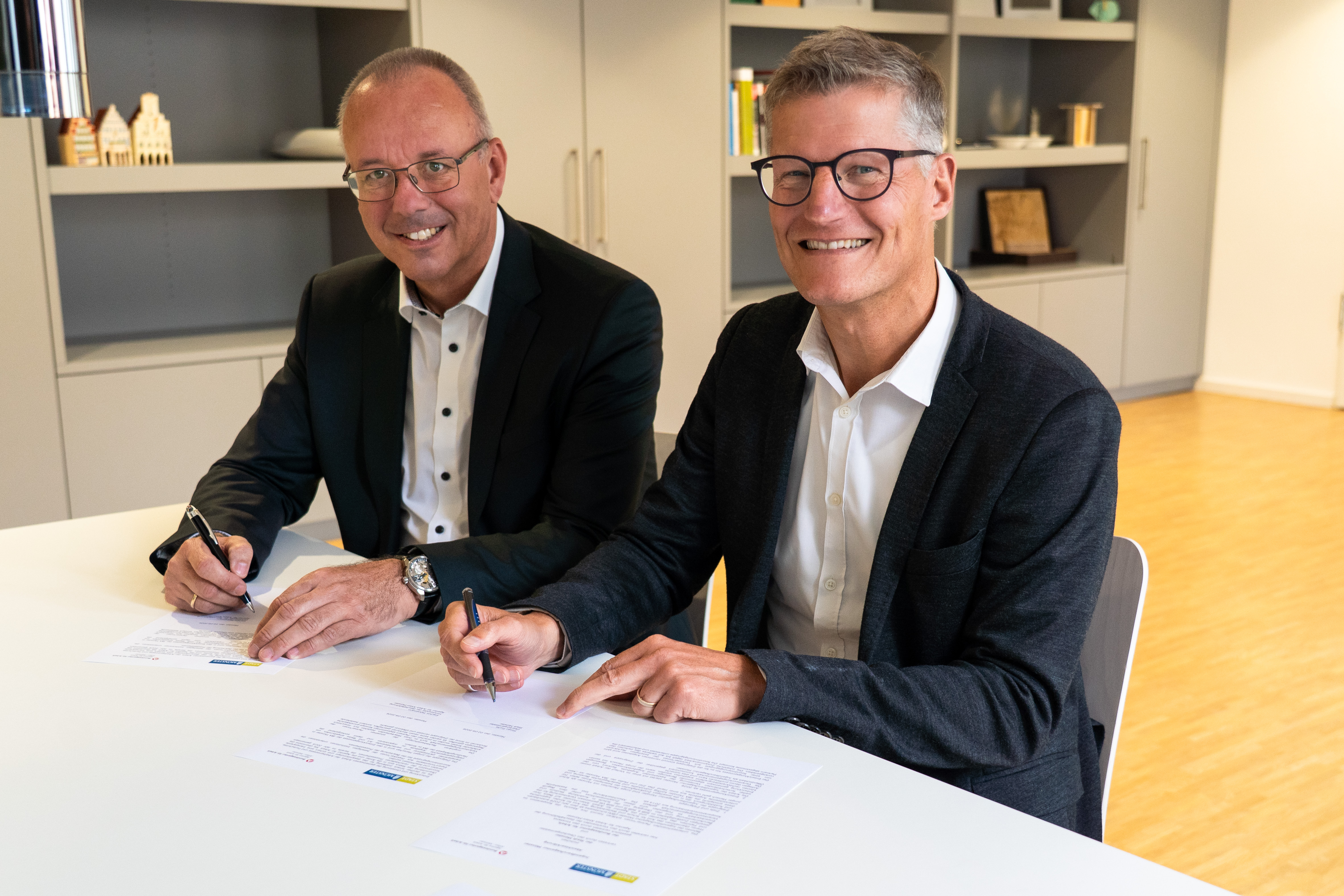 Zwei Personen sitzen nebeneinander an einem Tisch und schreiben auf Papier.