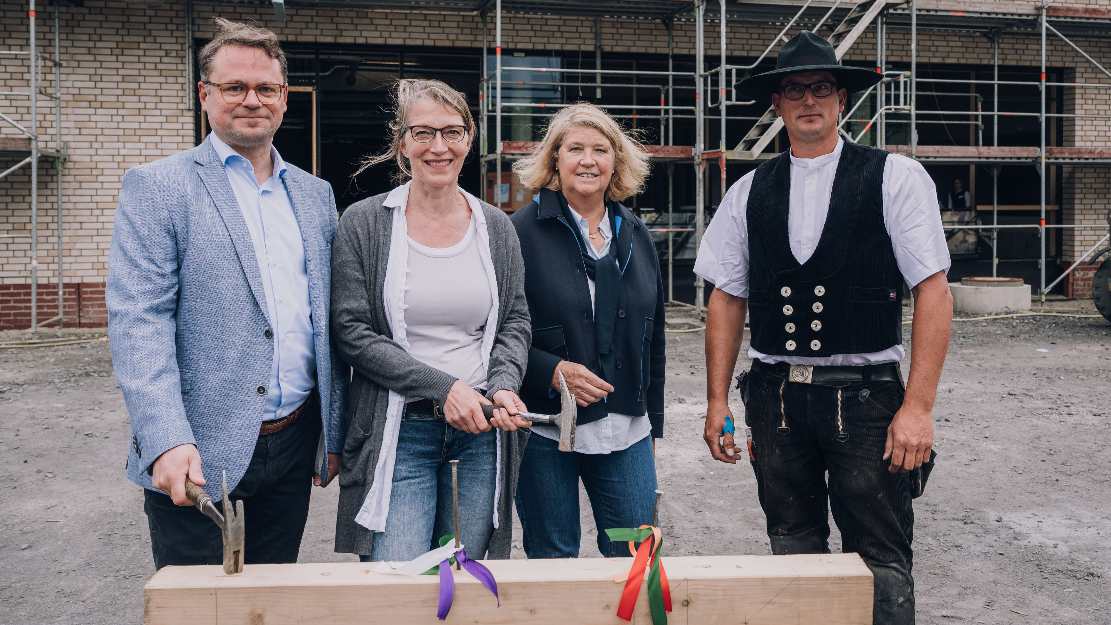 Bezirksbürgermeister Stephan Brinktrine, Bettina Haack, Projektleiterin Hanne Silies  und Zimmermann Sven Hüls schlagen beim Richtfest auf einen Nagel in einem Holzstamm ein 