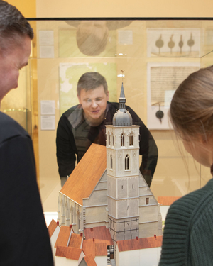 Drei Museumsgäste schauen sich das Modell der Lambertikirche in der Vitrine an