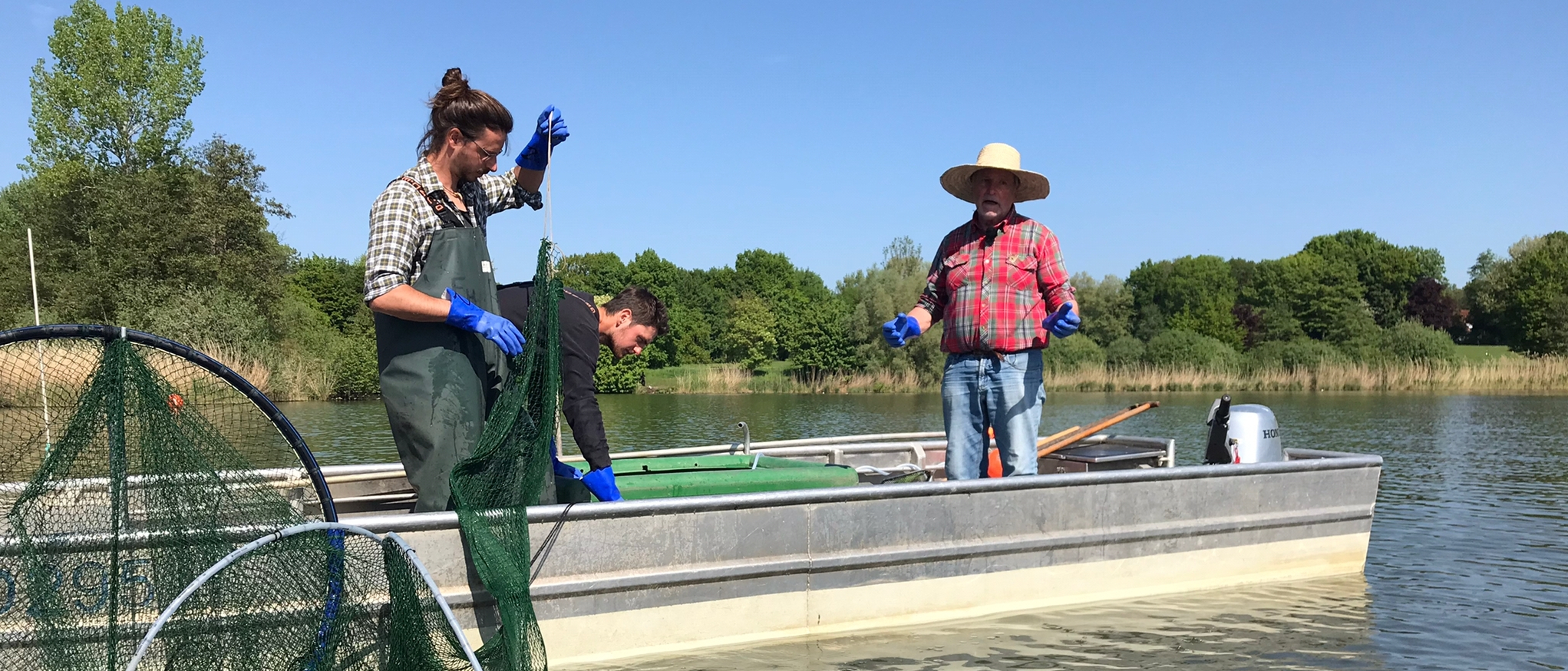 Drei Männer auf einem Boot mit Netzen zur Befischung auf dem Aasee