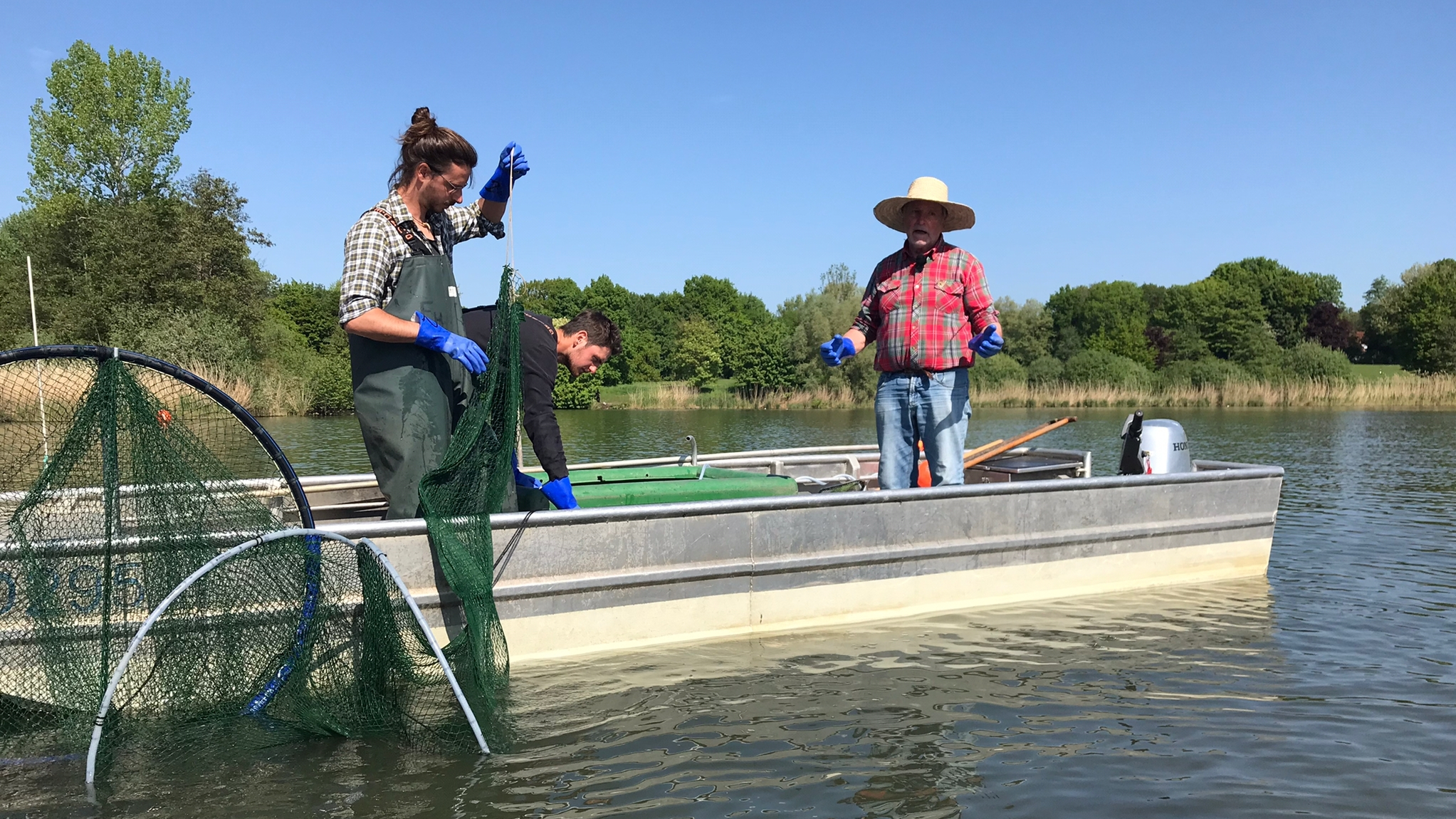 Drei Männer auf einem Boot mit Netzen zur Befischung auf dem Aasee