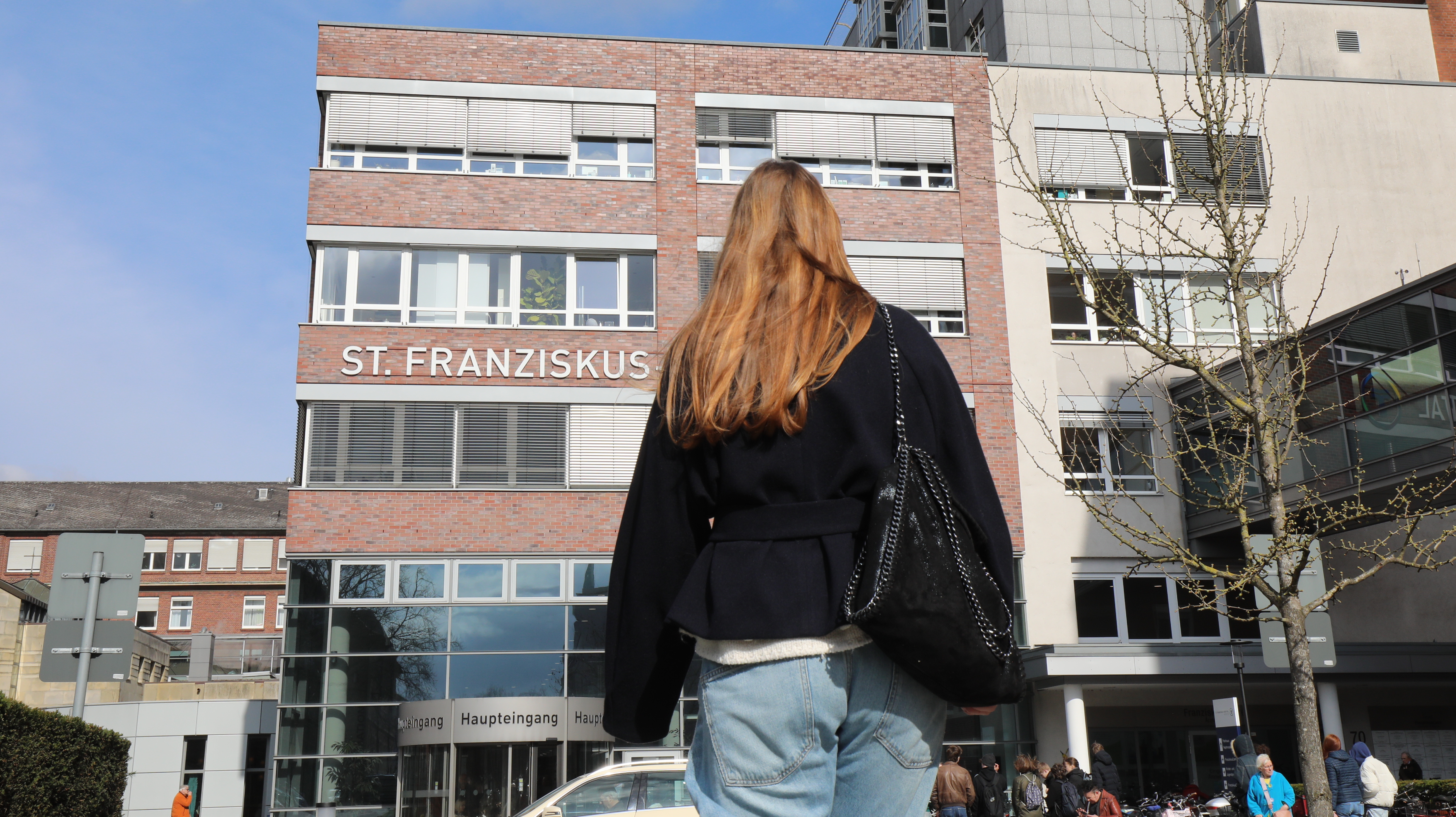 Eine junge Frau geht auf ein Krankenhaus zu.