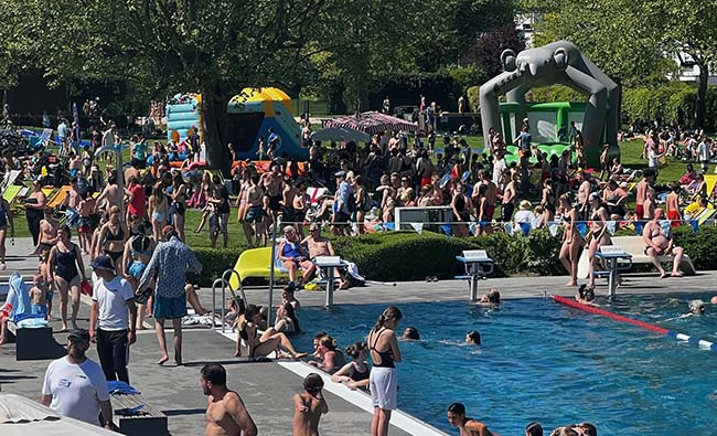Besucher im vollen Freibad Coburg, im Vordergrund das Schwimmbecken und der Rand, im Hintergund die Wiese mit Bäumen