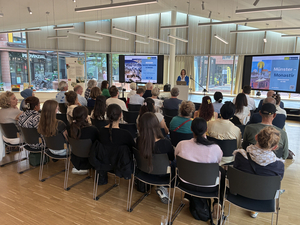 Gespräch mit dem Auswärtigen Amt, viele Menschen sitzen im Saal, im Hintergrund hält eine Frau einen Vortrag
