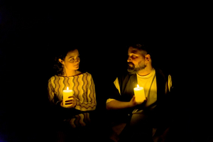 Eine Schauspielerin und ein Schauspieler stehen nur bei Kerzenschein auf der Bühne. Sie halten jeweils eine brennende Kerzen in der Hand.en