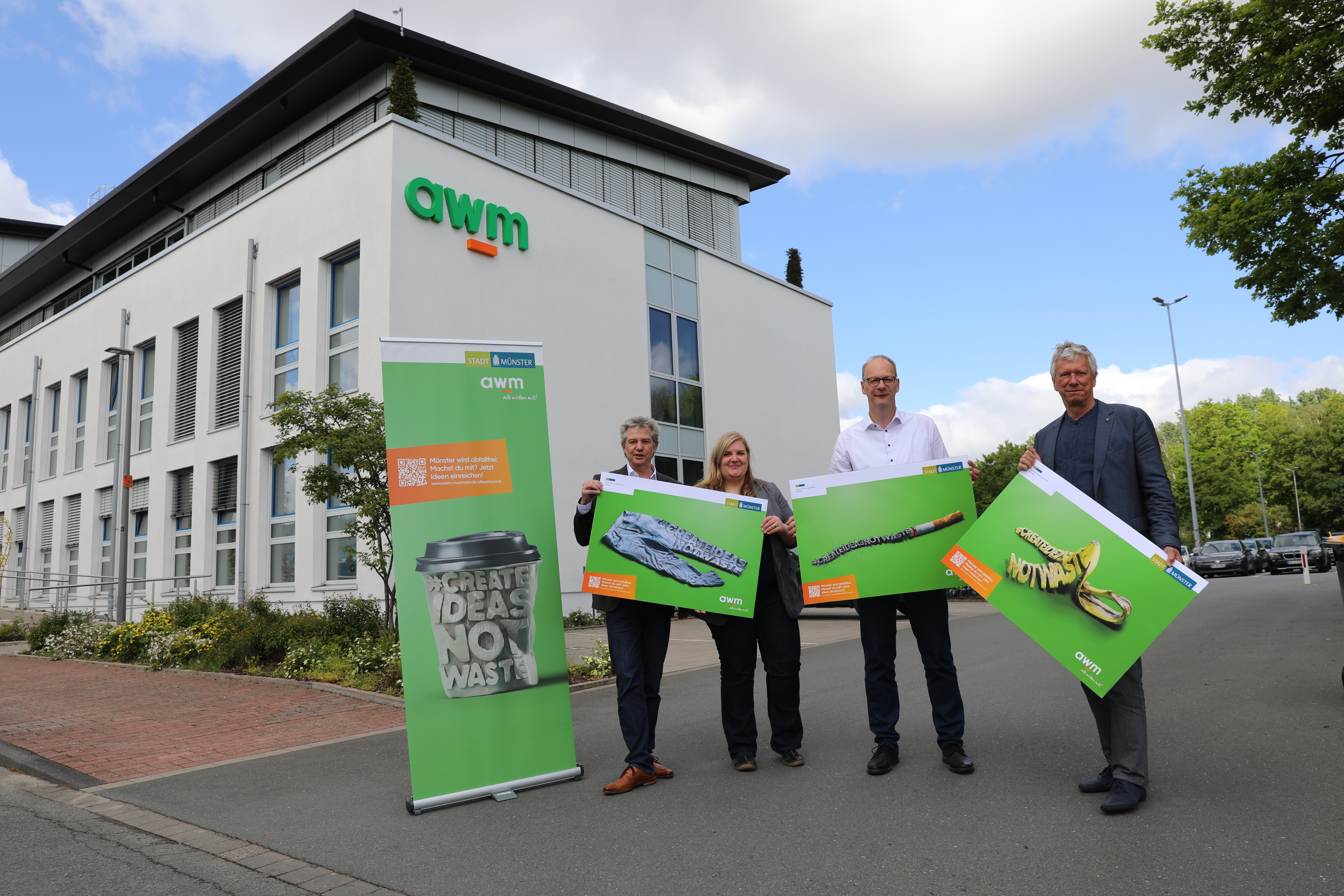 Personengruppe mit Motiven des awm-Ideenwettbewerbs vor dem awm-Verwaltungsgebäude