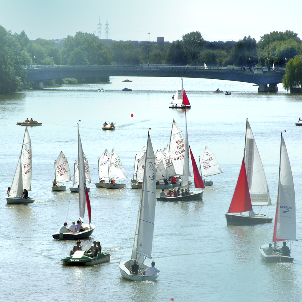 Auf dem Aasee in Münster fahren diverse Segel- und Tretboote in verschiedene Richtungen.
