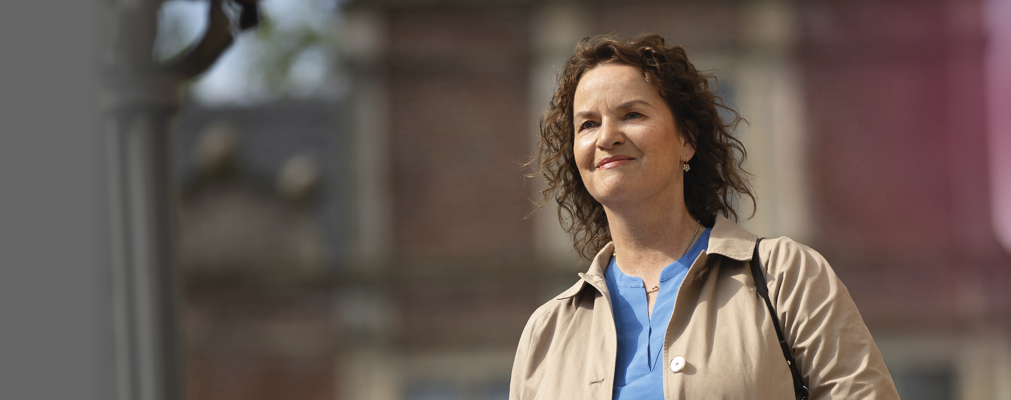 Frau mit Locken und heller Jacke schaut in die Kamera.