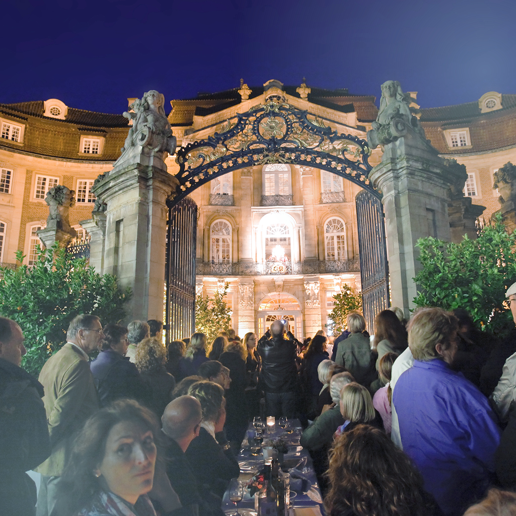 Menschen sitzen bei einer Open-Air-Veranstaltung an Tischreihen vor dem Erbdrostenhof in Münster.