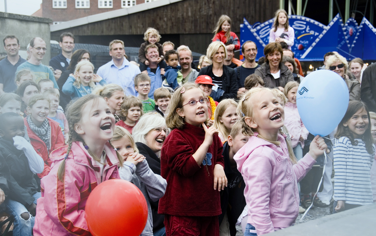 Viele lachende Kinder stehen vor einer Bühne auf dem Hafenfest in Münster.
