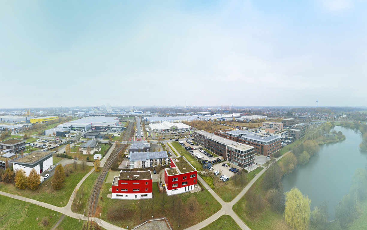 Ein Blick von oben über das Gewerbegebiet Loddenheide mit einem kleinen See und der dahinterliegenden Stadt Münster bis zum Fernsehturm.