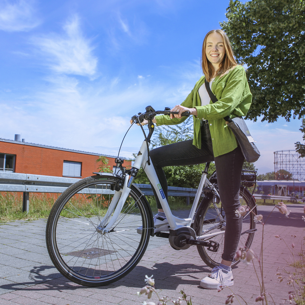Eine Frau trägt ein grünes Hemd und sitzt auf einem E-Fahrrad, welches mit dem Stadt Münster Logo bedruckt ist.