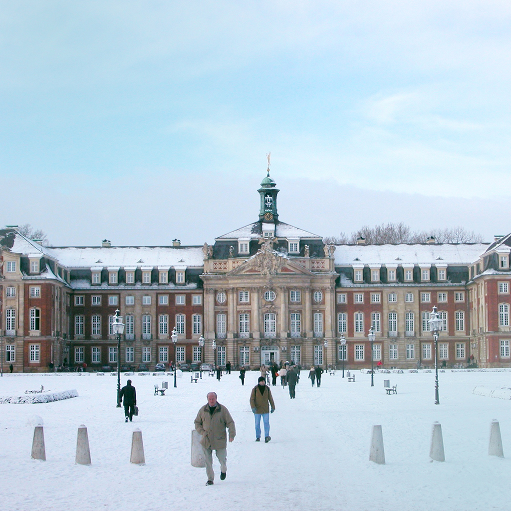 Hinter einem schneebedeckten Platz sieht man unter blauem Himmel das Schloss in Münster.