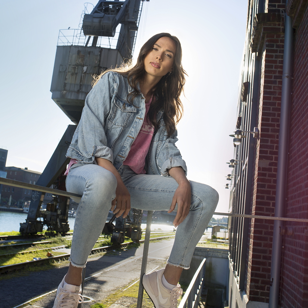 Eine junge Frau sitzt lässig auf dem Geländer vor dem Münsteraner Hafenkran und post selbstbewusst in die Kamera.