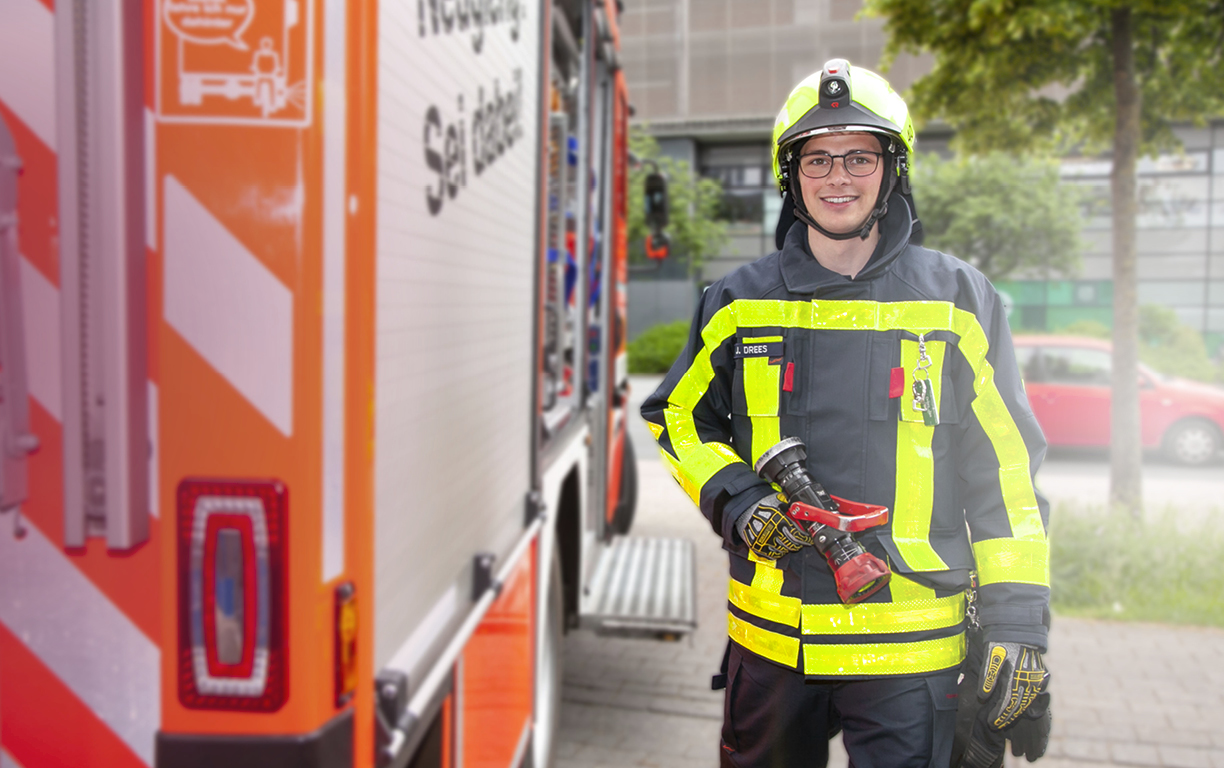 Ein junger Mann in Einsatzkleidung der Feuerwehr vor einem Feuerwehrauto