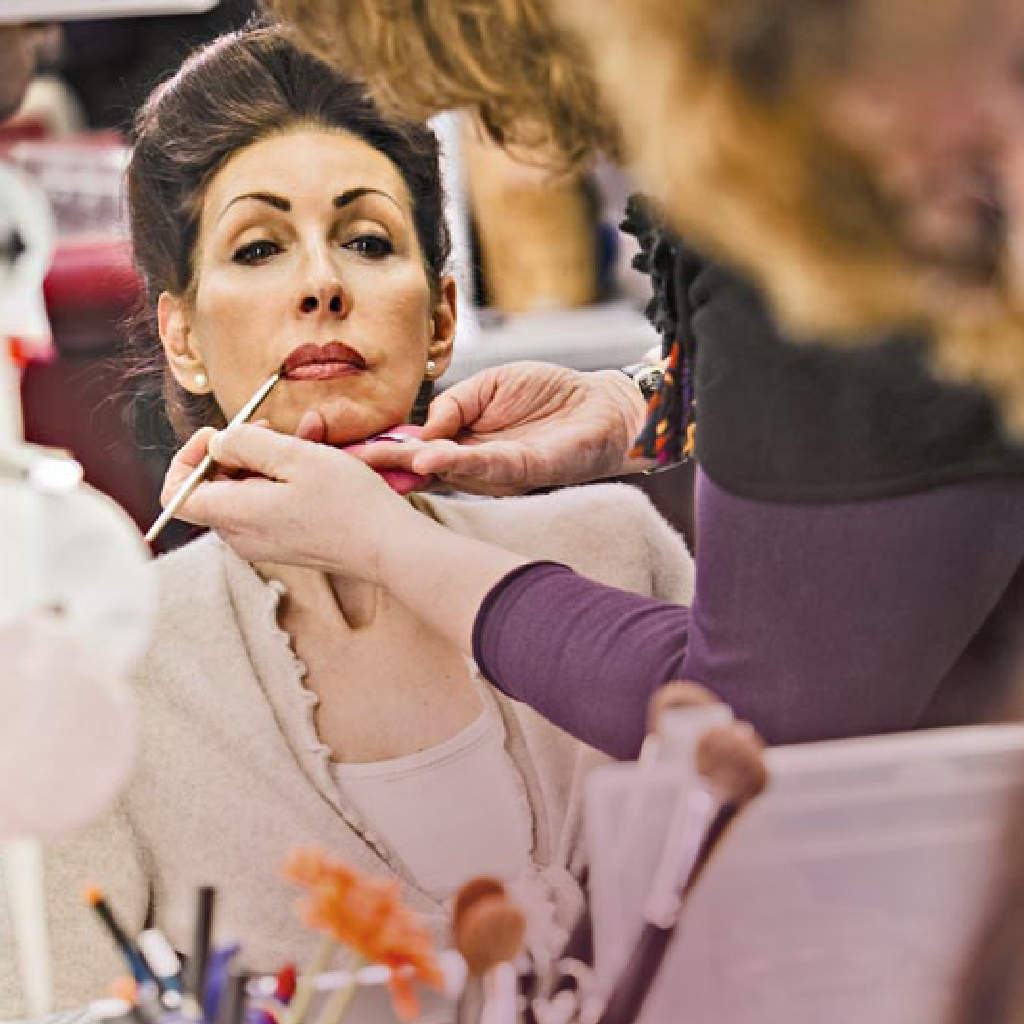 Eine unscharf fotografierte Maskenbildnerin schminkt eine Schauspielerin für ein Theaterstück im Theater Münster.