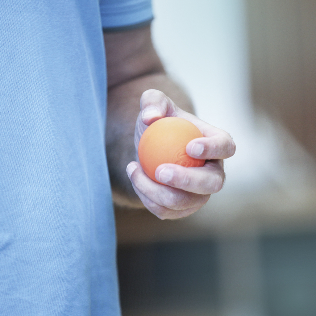 Ein Mann trägt ein hellblaues Poloshirt und hält in seiner linken Hand einen orangen Gummiball.