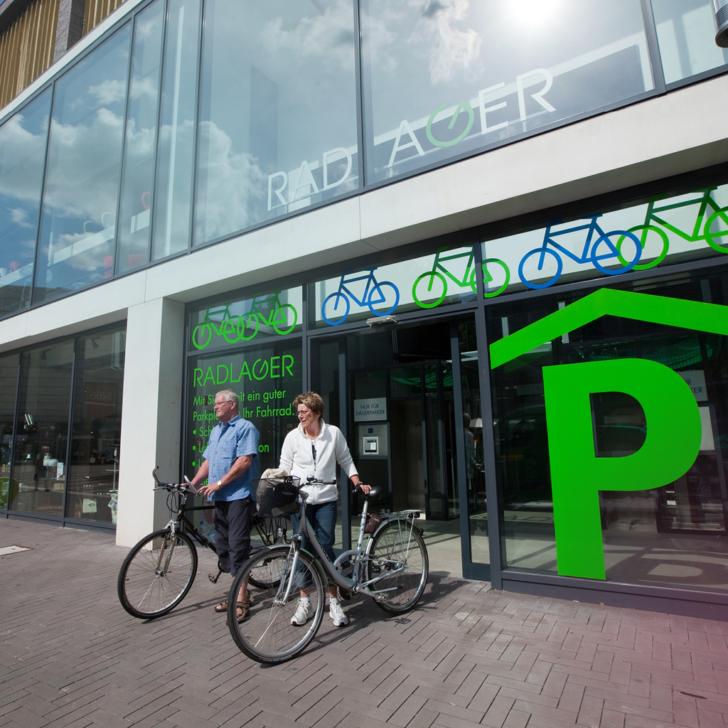 Ein Mann und eine Frau kommen mit Ihren Fahrrädern aus einer Radstation in der Münsteraner Innenstadt.