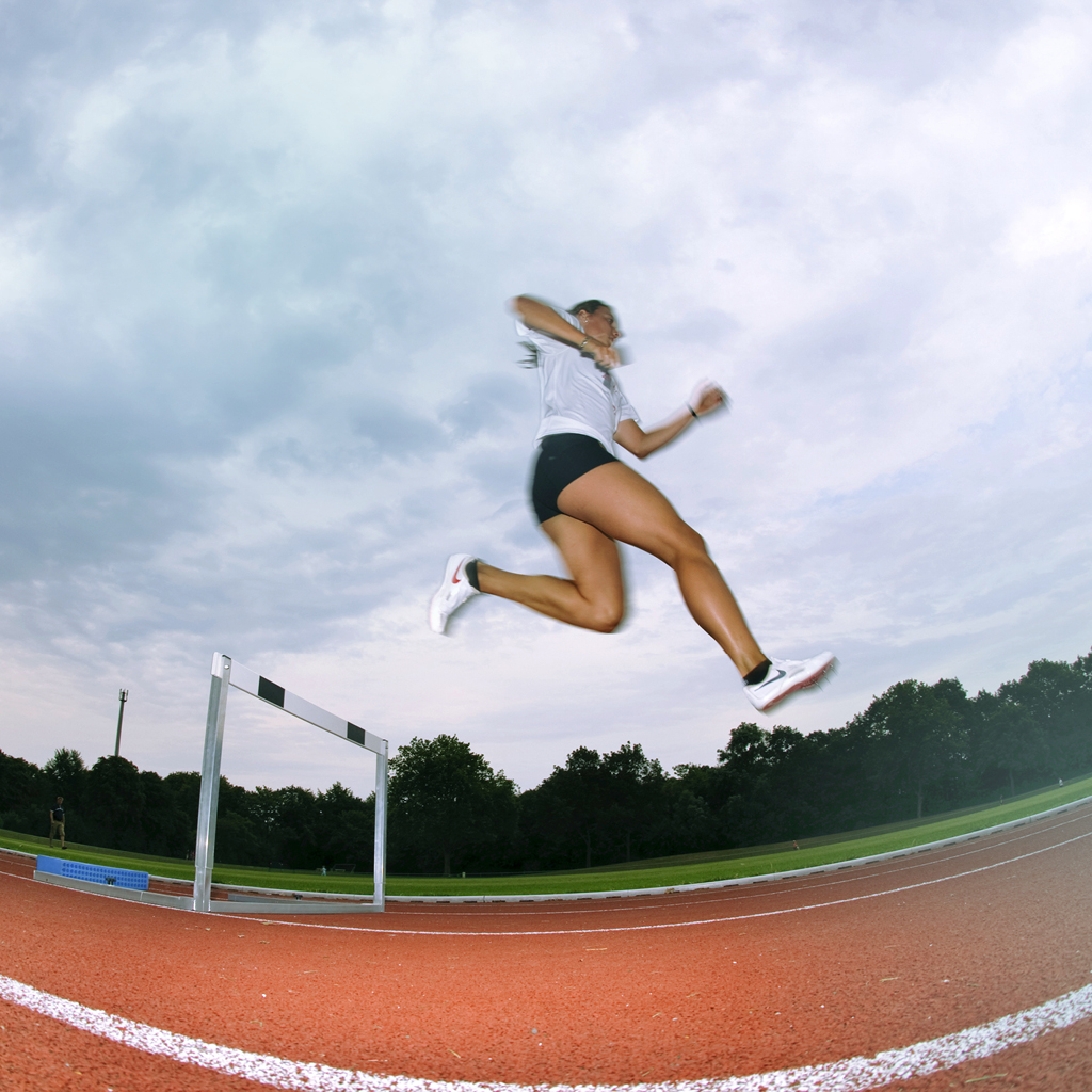 Eine junge Frau hüpft elegant über eine Hürde auf einer Sportlaufbahn der Stadt Münster.
