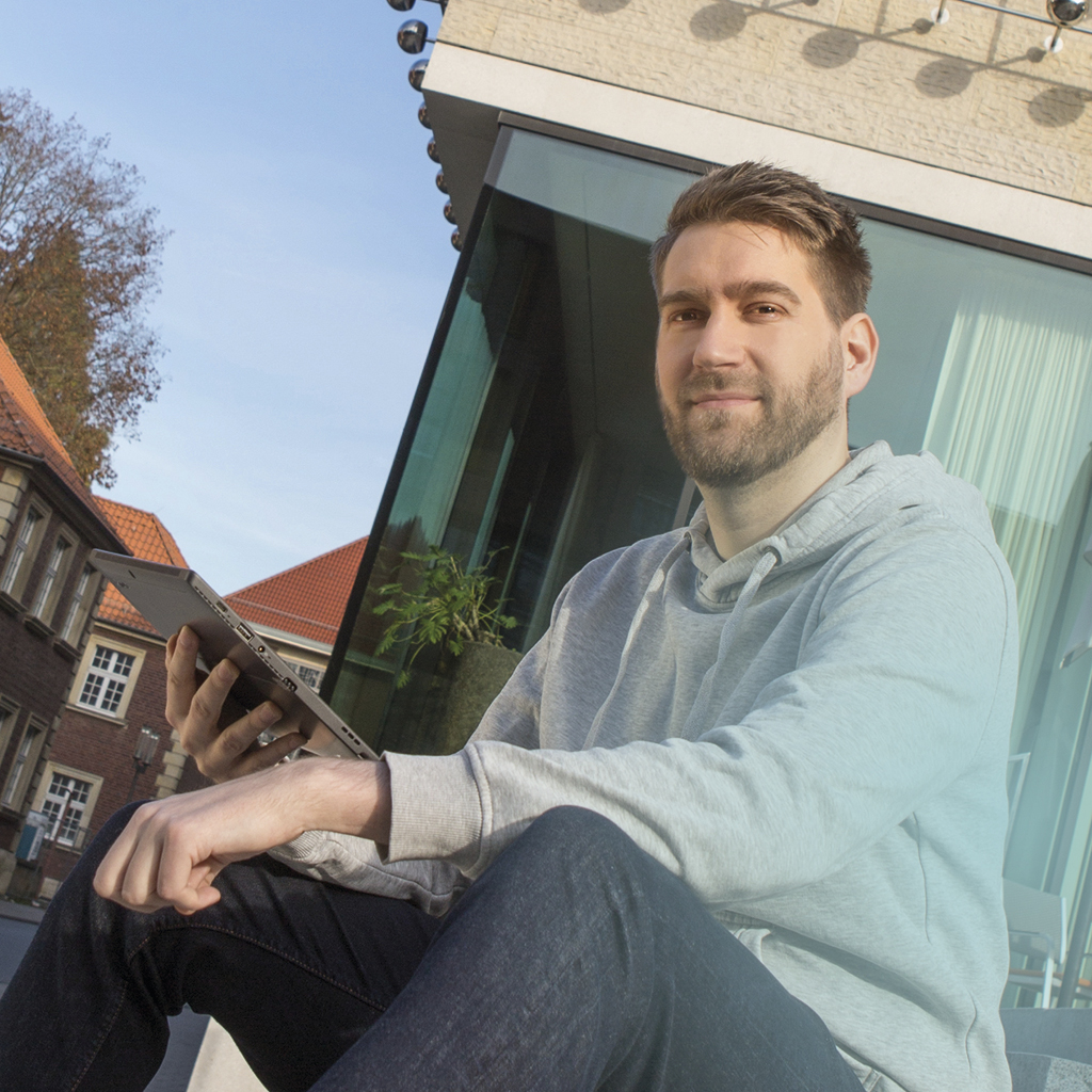 Ein Mitarbeiter der citeq sitzt auf der Treppe vor dem LWL-Museum und kann dank seines Tablet von dort aus arbeiten