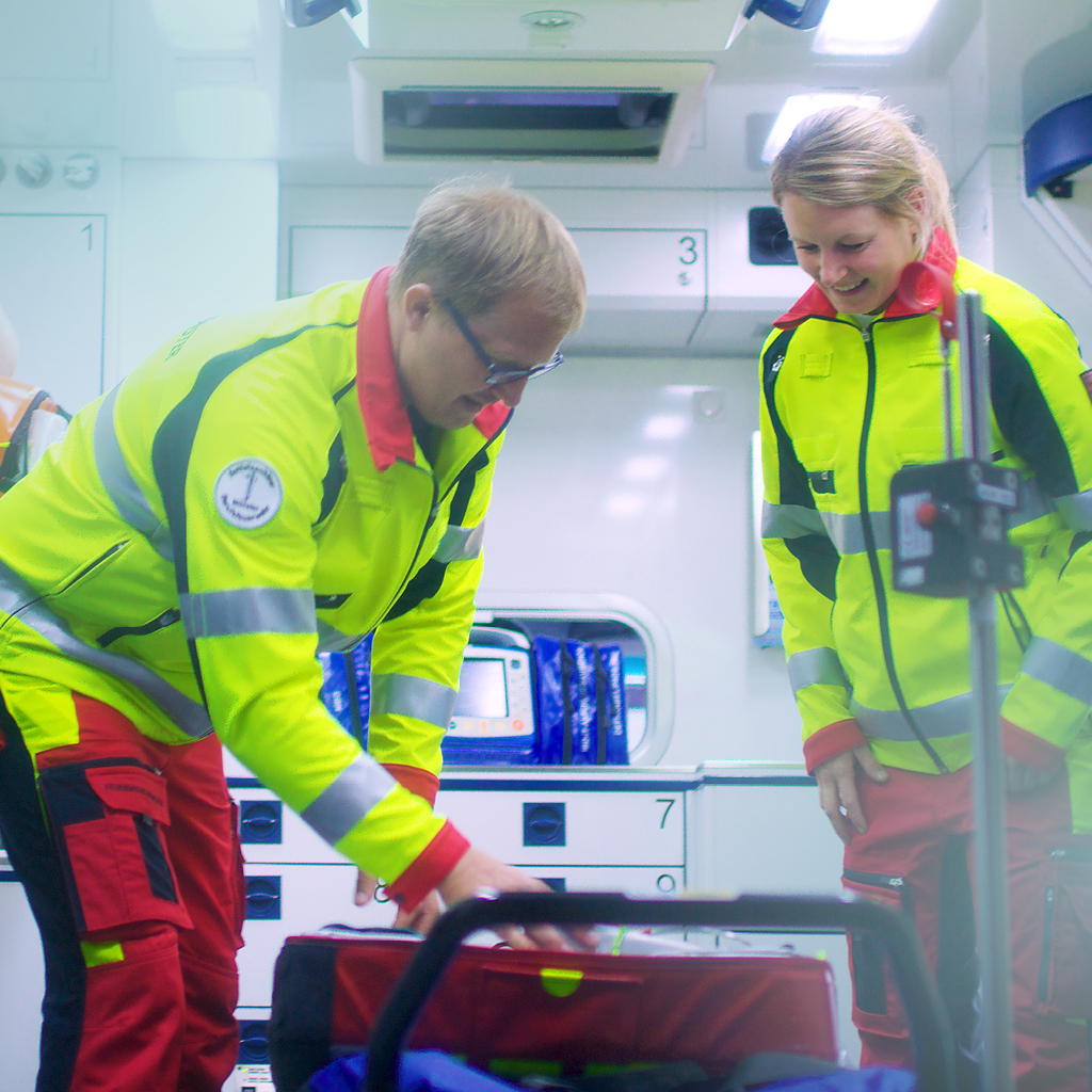 Eine Frau und ein Mann in gelben Sicherheitsjacken befinden sich im Innern eines Rettungswagens und bereiten etwas vor.