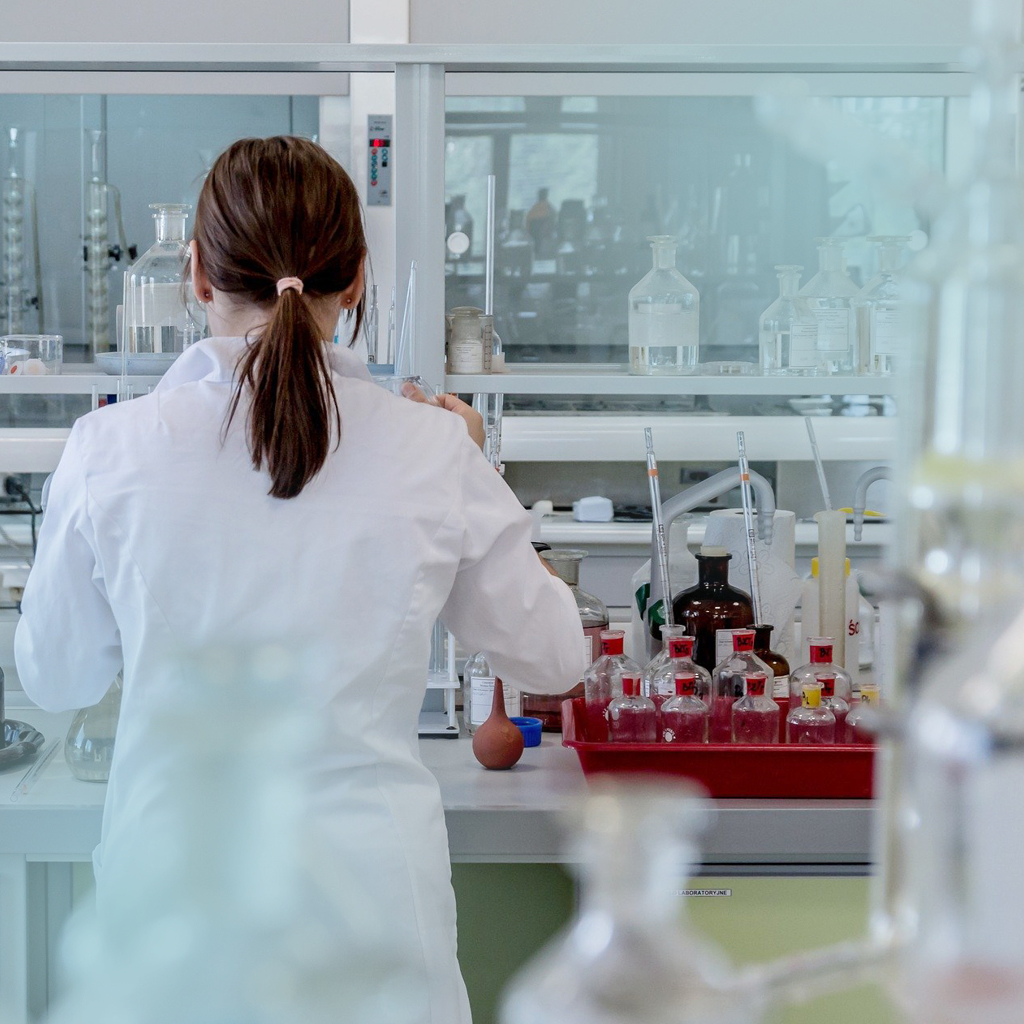 Eine Frau steht mit dem Rücken zum Betrachter in einem Labor und ist in hellblauer Schutzkleidung